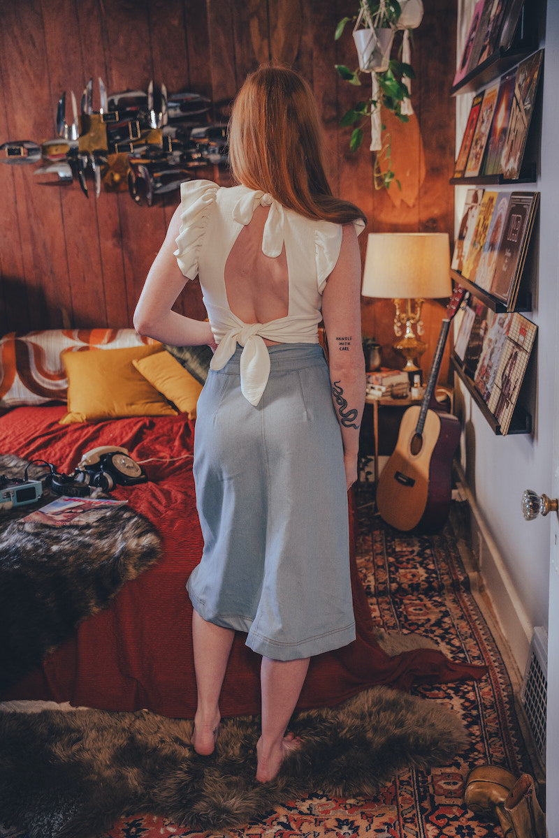 Woman standing in a cozy room with a guitar and books on the wall
