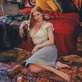Woman sitting on a patterned rug in a cozy room with a bed and plants.