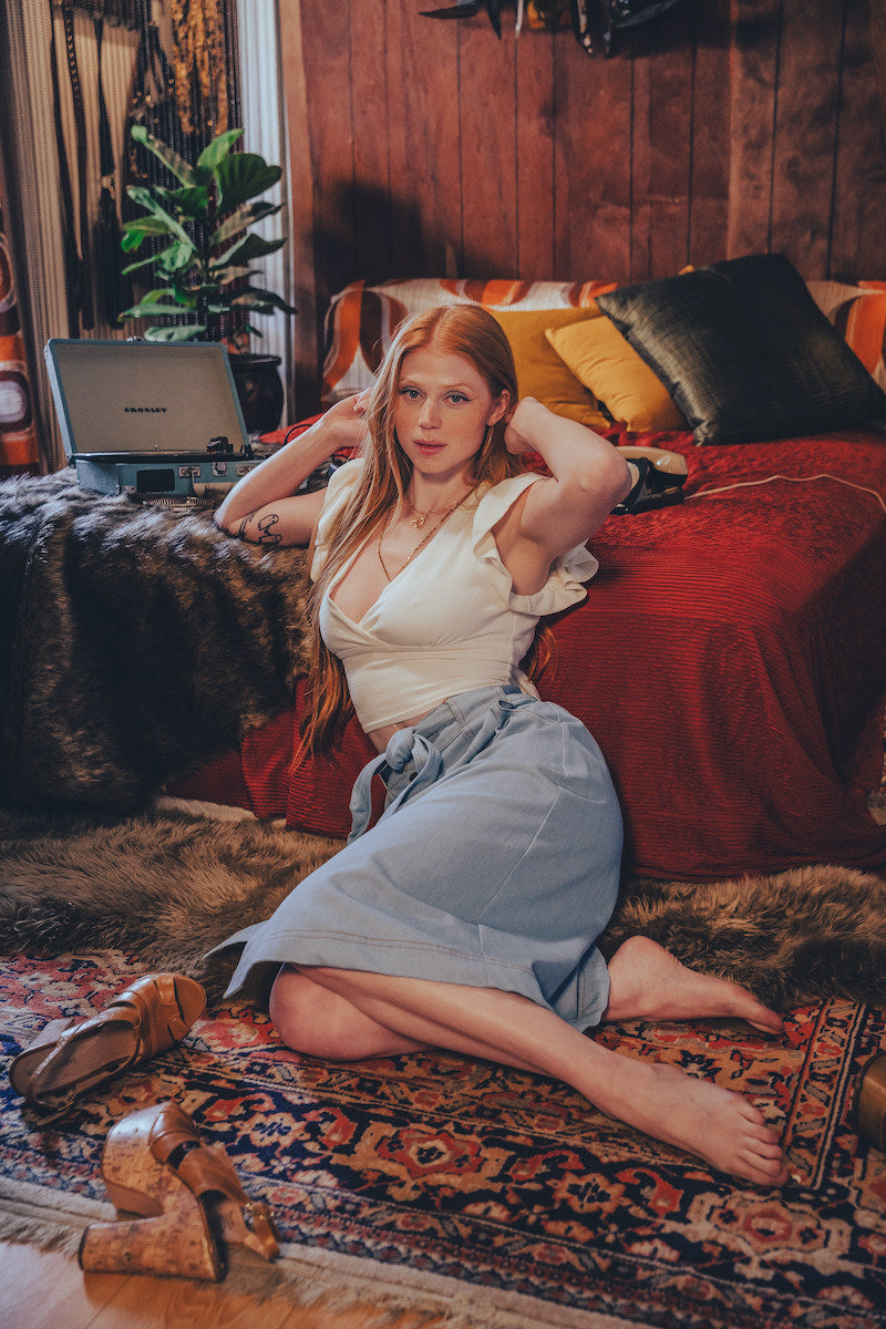Woman sitting on a patterned rug in a cozy room with a red couch and laptop.