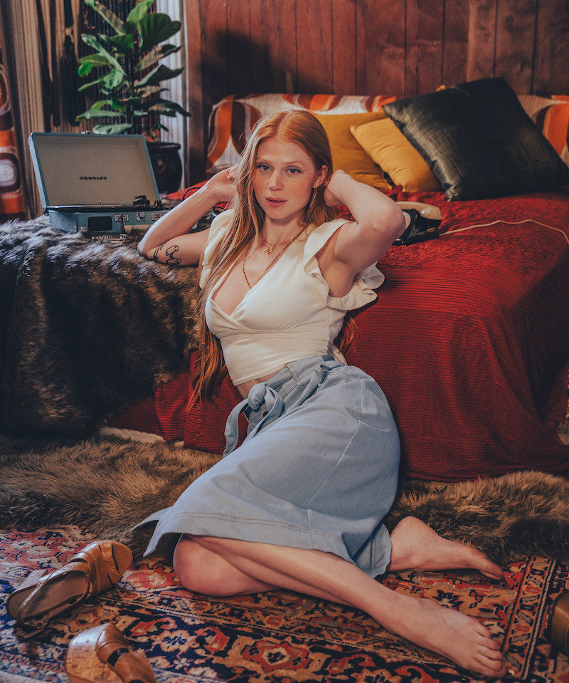 Woman sitting on a patterned rug in a cozy room with a red couch and laptop.