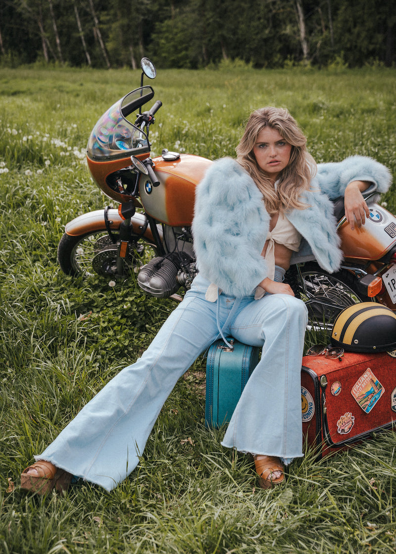 Woman sitting on a suitcase next to a motorcycle in a grassy field wearing Soul Sister since 1969