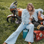 Woman sitting on a suitcase next to a motorcycle in a grassy field wearing Soul Sister since 1969