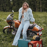 Woman in a light blue outfit sitting on an orange motorcycle in a forest setting wearing Soul Sister since 1969