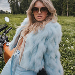 Woman in a light blue fur coat and sunglasses sitting on a motorcycle in a field wearing Soul Sister since 1969.