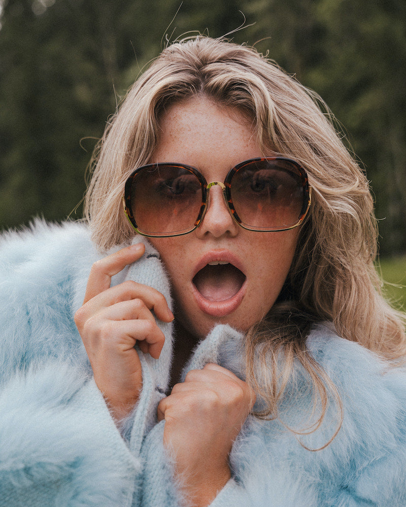 Person wearing sunglasses and a light blue fur coat with a blurred natural background wearing Soul Sister since 1969