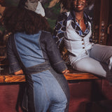 Two women sitting at a bar, one wearing a denim jumpsuit and the other in a patterned outfit.