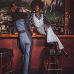 Two women in vintage clothing sitting at a bar with horse mural in the background