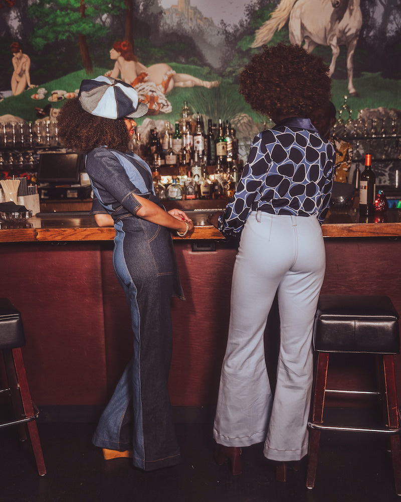 Two people standing at a bar with a vintage mural in the background
