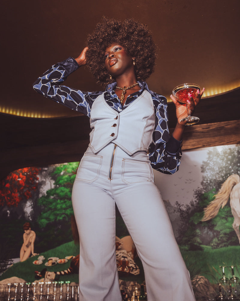 Woman in a stylish outfit holding a drink against a mural background