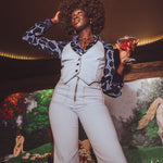 Woman in a stylish outfit holding a drink against a mural background