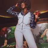 Woman in a stylish outfit holding a drink against a mural background