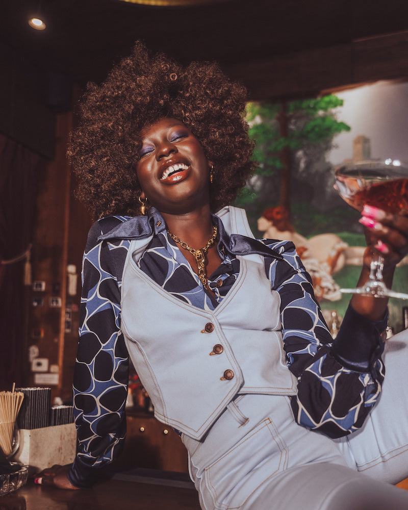 Woman in a stylish outfit holding a cocktail in a bar setting