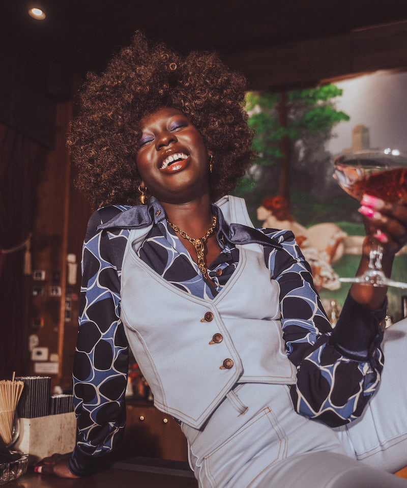 Woman in a stylish outfit holding a cocktail in a bar setting