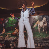 Person in a pale blue retro 70s outfit standing in front of a decorative wall with horse paintings.