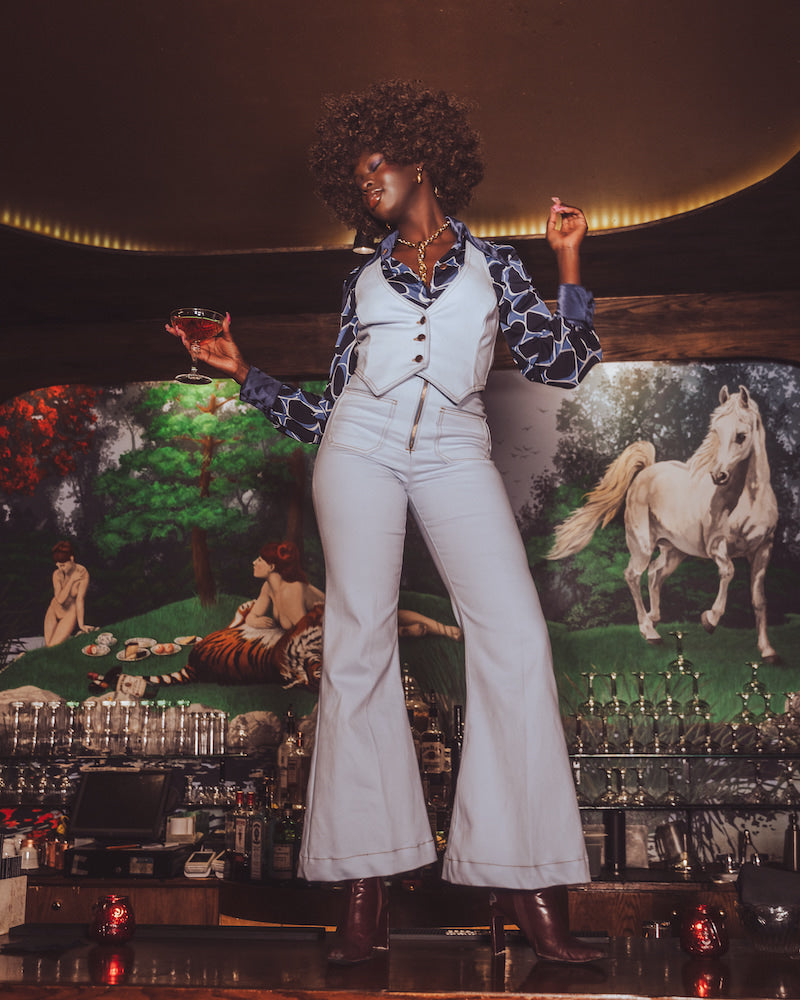 Person in a stylish outfit standing in front of a colorful mural with animals.