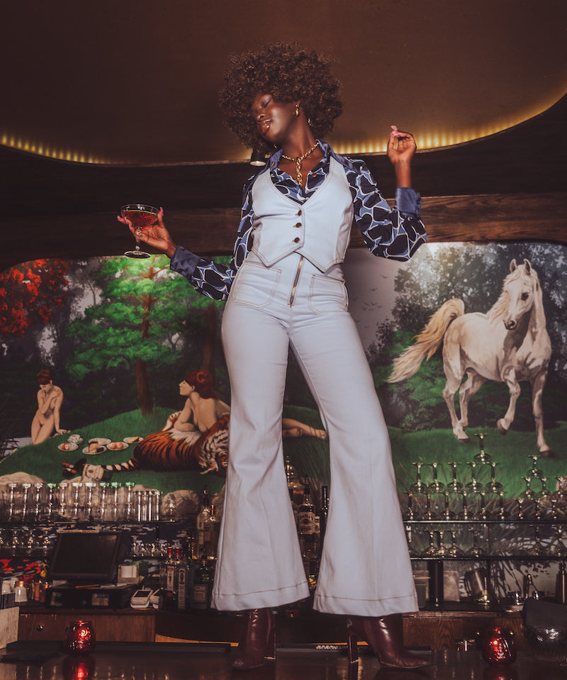 Person in a stylish outfit standing in front of a colorful mural with animals.