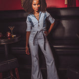 Woman in a light blue jumpsuit standing in a bar setting