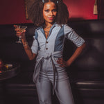 Woman in a gray jumpsuit holding a cocktail in a dimly lit room.