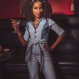 Woman in a gray jumpsuit holding a cocktail in a dimly lit room.