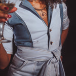 Person wearing a light blue outfit with a belt, holding a glass.