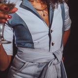 Person wearing a light blue outfit with a belt, holding a glass.