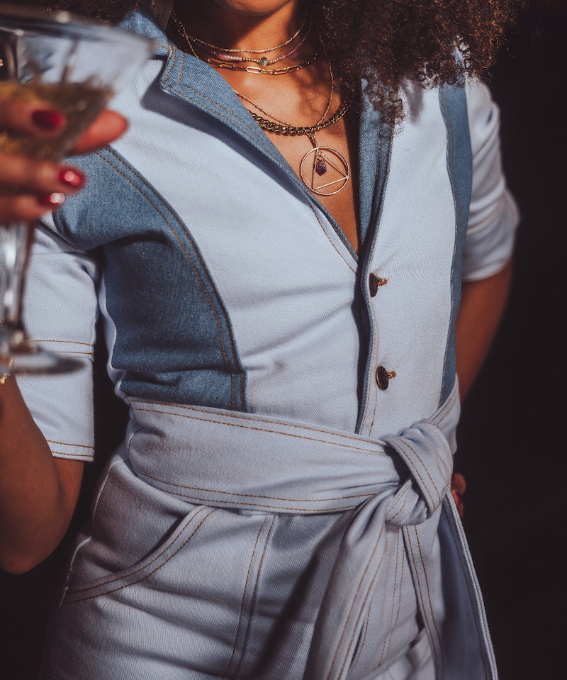 Person wearing a light blue outfit with a belt, holding a glass.