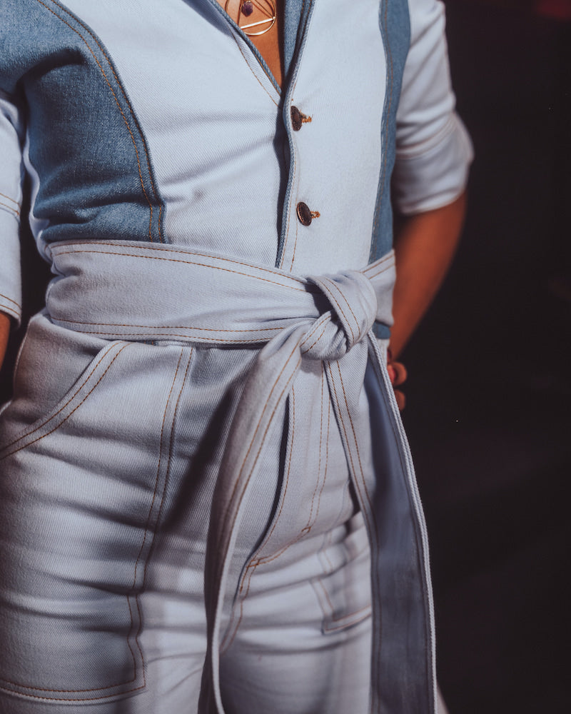 Light blue jumpsuit with a belt worn by a person, against a dark background