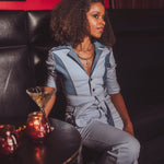 Woman in a gray outfit sitting on a dark leather couch with candles on a table.