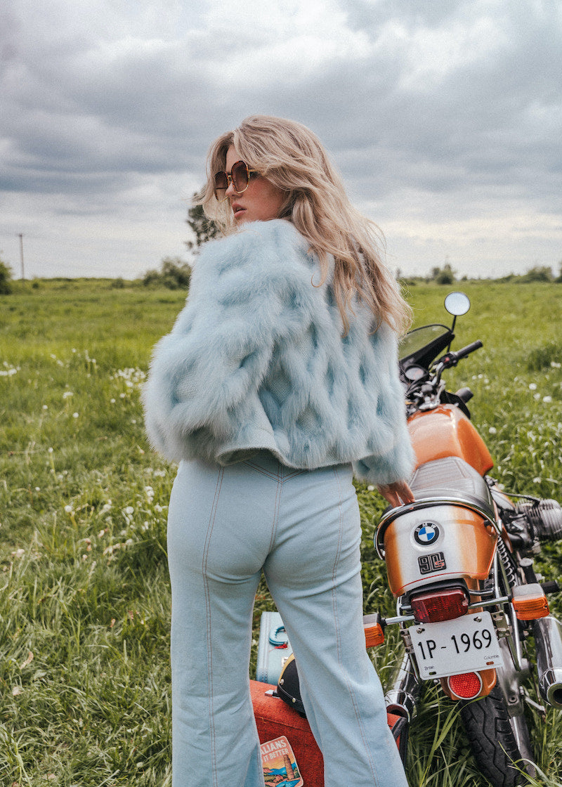 Woman in a field with a motorcycle, wearing a fur coat and sunglasses Soul Sister since 1969..