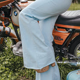 Person wearing light blue jeans sitting on a motorcycle with a suitcase nearby Soul Sister since 1969..