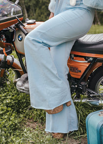 Person wearing light blue jeans sitting on a motorcycle with a suitcase nearby Soul Sister since 1969..