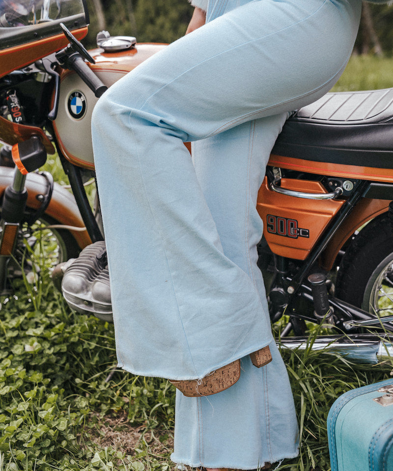 Person wearing light blue jeans sitting on a motorcycle with a suitcase nearby Soul Sister since 1969..