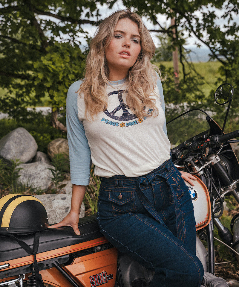 Woman sitting on a motorcycle wearing a peace sign t-shirt with a scenic background Woman wearing a peace symbol shirt with text outdoors wearing Soul Sister since 1969