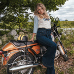 Woman sitting on a motorcycle in a natural setting with trees and grass wearing Soul Sister since 1969.