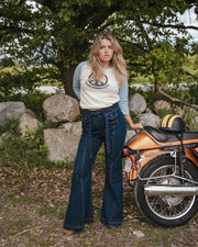 Woman standing next to a motorcycle in a natural setting with trees and rocks wearing Soul Sister since 1969..