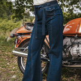 Person wearing blue jeans standing next to an orange motorcycle in a natural setting wearing Soul Sister since 1969.