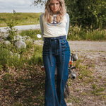 Woman in a white t-shirt and blue jeans standing next to a motorcycle in a natural setting wearing Soul Sister since 1969..