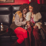 Two women sitting on a black leather couch in a room with red walls and a painting.