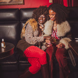 Two women sitting on a black leather couch in a room with red walls and a painting.