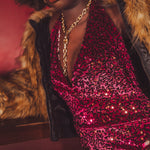 Person wearing a red sequin dress with a fur-lined coat against a dark background