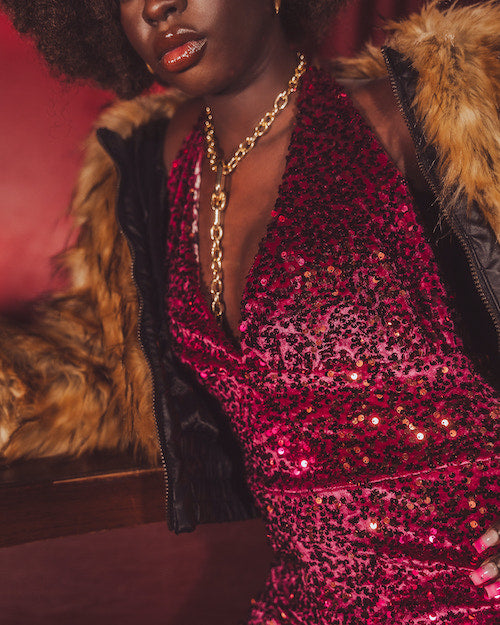 Person wearing a red sequin dress with a fur-lined coat against a dark background