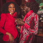 Two women in red and patterned outfits standing close together in a bar setting.