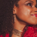 Close-up of a woman wearing gold jewelry with a red rose