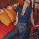 Woman sitting on a bed in a room with wooden walls and a guitar in the background