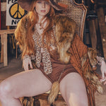 Woman in a vintage-style outfit with a large hat and fur trim sitting on a chair.