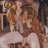 Woman in a vintage-style outfit with a large hat and fur trim sitting on a chair.
