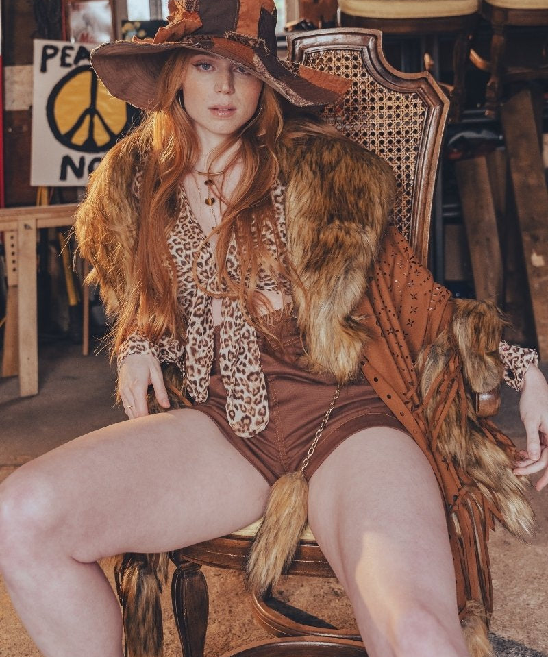 Woman in a vintage-style outfit with a large hat and fur trim sitting on a chair.
