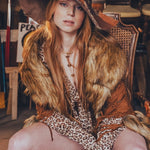 Person wearing a fur-trimmed outfit with a hat, sitting in a rustic setting.