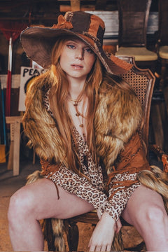 Person wearing a fur-trimmed outfit with a hat, sitting in a rustic setting.