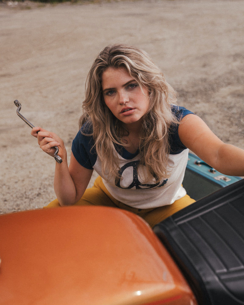 Woman holding a wrench next to a car in an outdoor setting 
